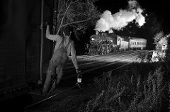 railroad crew riding a boxcar with a lantern as a passenger train passes in the background