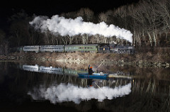 steam train and its reflection passes a fisherman in a rowboat