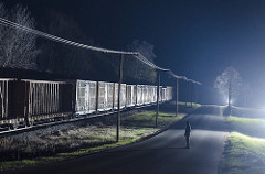 man standing in a rurual road watching freight train pass at night