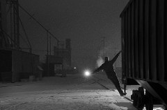 conductor rides a grain car over a crossing in a snow storm